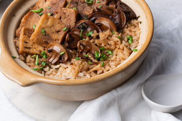 Overhead view vegan claypot rice with pan fried tofu, mushrooms and scallions, top view of crispy rice in a donabe on a marble countertop