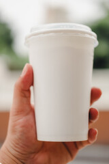 Hand holding plain white paper cup with lid