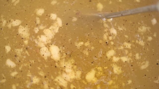 boiling, savory beef broth with spices and melting gelatin pieces being stirred with big metal spoon. close-up view cooking process for traditional rich beef jelly or savory aspic.