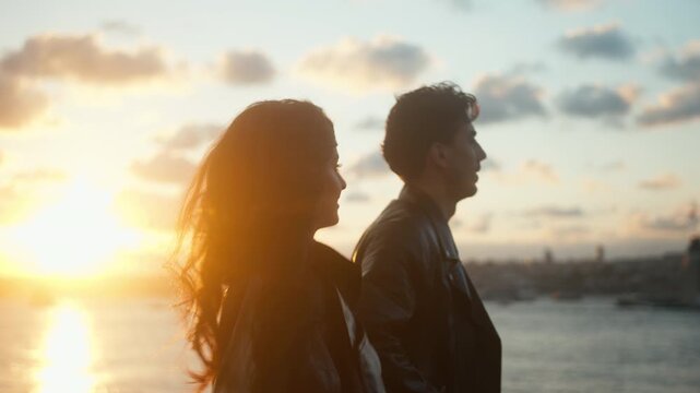Young couple stands side by side, admiring a beautiful sunset over the city skyline, sharing a peaceful and romantic moment together.
