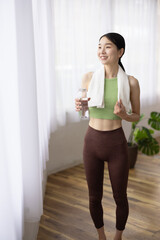 Smiling Japanese Woman in Yoga Wear Holding Water Bottle by the Window