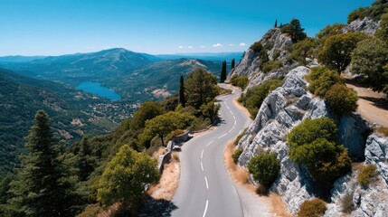 Winding Mountain Pass Road Cutting Through Lush Green Forest with Distant Lake and Blue Sky on a Sunny Day