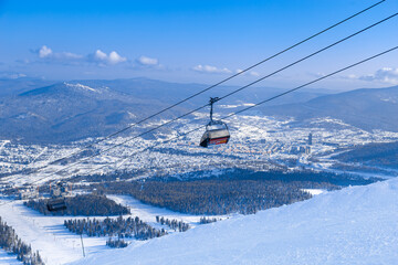 Panoramic View from Green mount on Sheregesh ski resort, Altai mountains. Active winter rest, white snow ski slopes, tracks and chairlift, clear blue sky and forest. Atmosphere of mountain holiday.