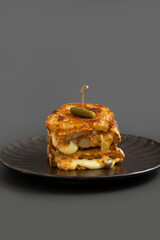 Crispy Chicken sandwich with Sourdough bread, Mozzarella cheese, CheddarCheese and spicy sauce on black plate.