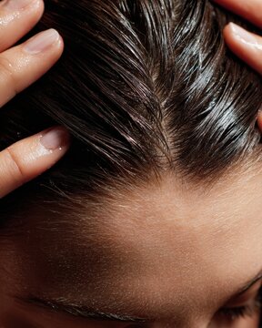 Close-up of hands applying nourishing scalp treatment with gentle massaging motion on parted healthy hair showing direct skin care for hair health and wellness routine concept