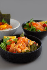 Salmon sashimi salad with green leaves, tomato and lemon on grey background.