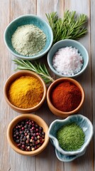 Top Down Overhead View Of Six Small Bowls Filled With Assorted Spices And Herbs Including Rosemary Sprigs On A Light Wooden Table Surface