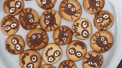 Close-up of Halloween chocolate cookies decorated like spiders with candy eyes and chocolate legs. Festive homemade treats for Halloween celebration, kids party, or autumn holiday.