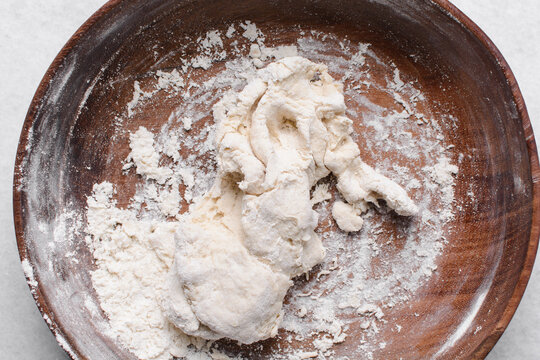 Overhead view of paratha dough being mixed in a wooden bowl, top view of flaky flatbread dough in a wood bowl, process of making paratha