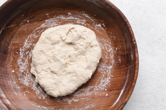 Overhead view of paratha dough being mixed in a wooden bowl, top view of flaky flatbread dough in a wood bowl, process of making paratha