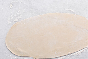 Overhead view of paratha dough being rolled out, top view of flaky flatbread dough, process of making paratha