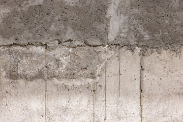 Rough textured concrete wall stands prominently in an outdoor setting. Weathered surface displays unique patterns and colors, capturing the essence of time and nature.