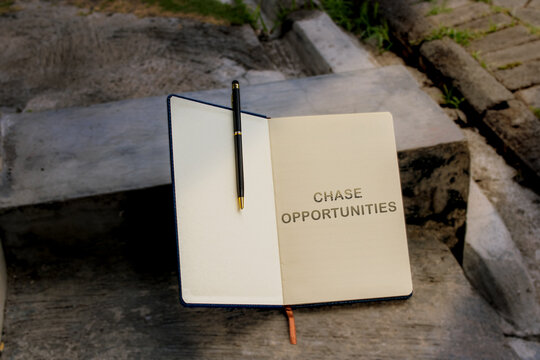 An open notebook with the financial maxim "CHASSE OPPORTUNITIES" written on one page, resting outdoors on rough concrete steps.