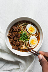 Overhead view of spicy noodle soup with beef chunks in a bowl, top view of tomato noodle soup with beef chunks