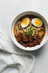 Overhead view of spicy noodle soup with beef chunks in a bowl, top view of tomato noodle soup with beef chunks