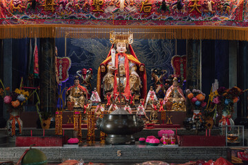 Fototapeta premium Golden statue of a deity sitting on a throne inside a chinese temple, surrounded by offerings and smaller statues
