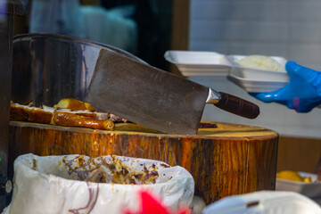Large sharp cleaver sitting next to roasted meat on wood cutting board