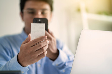 A man is using his cell phone to pay for something. He is holding a receipt in his hand