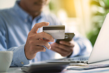 A man is holding a credit card and a cell phone, possibly using them to make a purchase