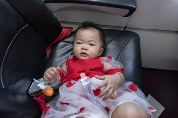 Baby girl sitting in airplane seat wearing pacifier holding toy