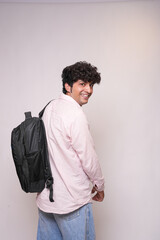 Happy indian college student with backpack standing isolated on white background. Smiling young asian adult boy looking at camera. Education concept.