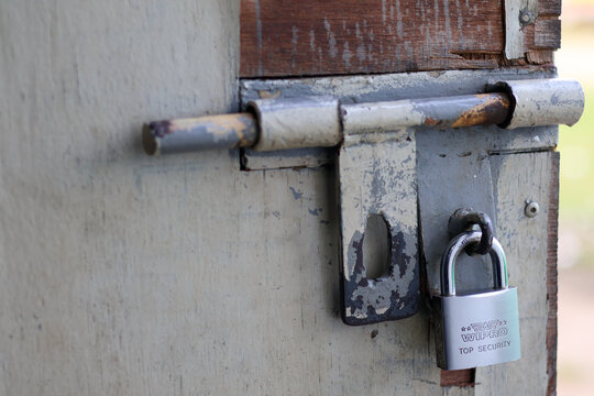 Balikpapan-indonesia October 28, 2025 Close-up of an old, weathered wooden door secured by a heavy-duty metal slide bolt and a shiny new padlock, symbolizing security, rustic aging, and protection.