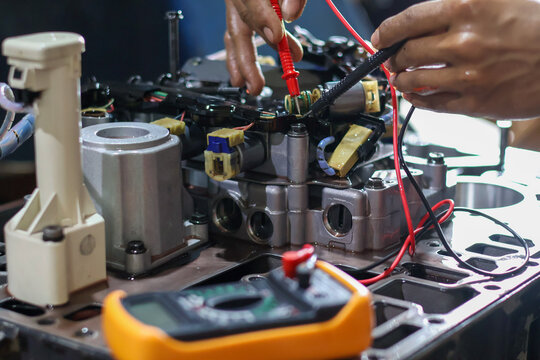 Hands of a technician using a multimeter to check the wiring and solenoid components of an automatic transmission valve body during diagnostic testing and repair.