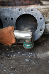 Worker using a pneumatic die grinder with an abrasive wheel to smooth and polish the rough surface of a heavy-duty cast metal industrial pump or turbocharger casing.