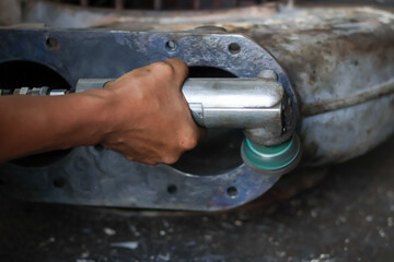 Worker using a pneumatic die grinder with an abrasive wheel to smooth and polish the rough surface of a heavy-duty cast metal industrial pump or turbocharger casing.