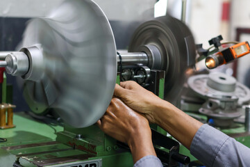 Close-up of a worker operating a dynamic balancing machine, adjusting the high-speed rotating turbine or fan component in a heavy industrial factory environment.