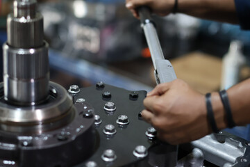 Mechanic's hands tightening a series of nuts on a heavy metal machine component using a torque wrench during precise assembly or industrial equipment repair.