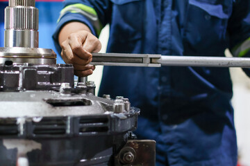 Mechanic's hands tightening a series of nuts on a heavy metal machine component using a torque wrench during precise assembly or industrial equipment repair.