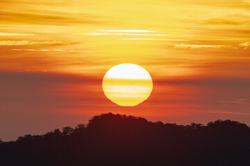Big sun setting behind the hills at dusk with orange and red sky