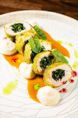A colorful chicken dish showcases spinach filling, elegantly plated with sauces and garnishes