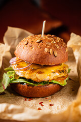 Juicy chicken burger stacked with greens, cheese, and colorful toppings served on parchment paper