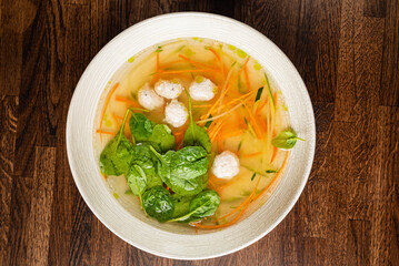 Bowl of broth with meatballs, fresh spinach, and colorful veggies on a wooden table
