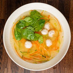 Delicate meatballs float in a clear broth with vibrant carrots and fresh spinach, inviting comfort