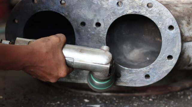 Worker using a pneumatic die grinder with an abrasive wheel to smooth and polish the rough surface of a heavy-duty cast metal industrial pump or turbocharger casing.
