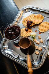 Delicious waffles topped with berry jam, sugar cubes, and a coffee pot on a shiny tray