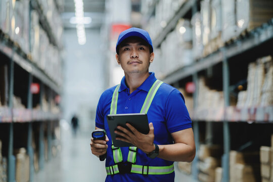A man in a blue shirt and safety vest is holding a tablet and a barcode scanner. He is standing in a warehouse