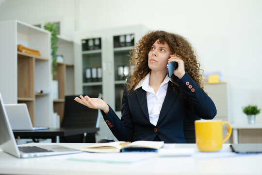 Confused businesswoman talking on phone at modern office desk with documents