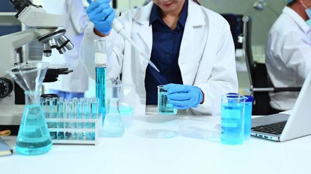 Closeup of Asian scientists using pipette and blue liquids in a modern lab, showcasing biotechnology, chemistry, and scientific innovation.