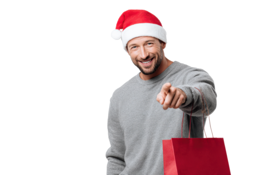 Smiling man wearing Santa hat and gray sweater holding red shopping bag while pointing forward, representing cheerful Christmas spirit, gift shopping, and holiday joy