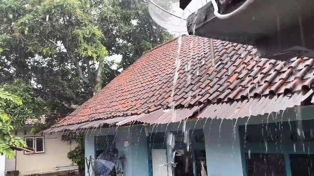 Heavy rain flowing over the zinc roof of a house in a beautiful green village in the afternoon