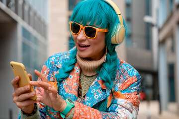 Young woman with turquoise hair enjoys music while checking her phone in a vibrant outdoor city setting
