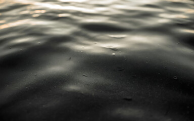 Closeup of dark, rippling water surface with subtle reflections of light