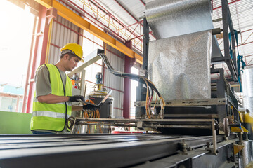 Engineer in safety gear using a laptop to monitor and control a roll forming machine producing aluminum foil or thermal insulation sheet in a factory.