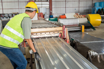 Industrial worker in safety uniform manually guiding a newly manufactured corrugated metal sheet from the heavy roll forming machine.