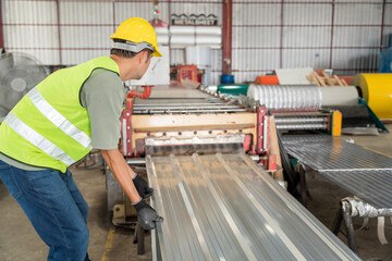 A Focused industrial worker in high-vis vest and hard hat manually handling a finished metal sheet from the roll forming machine in a factory.