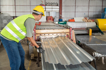 A Worker in reflective vest and hard hat manually guiding a finished corrugated metal sheet from...